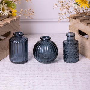 May include: Three blue glass vases with different textures. The vase on the left has vertical ridges, the middle vase has horizontal ridges, and the vase on the right has a diamond pattern.