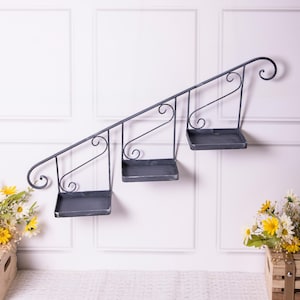 May include: A black metal wall-mounted shelf unit shaped like a staircase with three shelves. The shelves are made of metal and have a distressed finish.