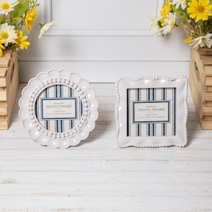 Può includere: Una cornice portafoto rotonda bianca smerlata e una cornice portafoto quadrata bianca con perline, entrambe con un inserto a righe blu e bianche con il testo PHOTO FRAME 4 x 4 10CM X 10CM APPROX. Le cornici hanno una finitura lucida.