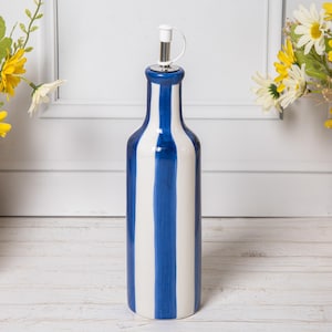 Könnte beinhalten: Eine Keramik-Ölflasche mit blau-weißem Streifendesign. Die Flasche hat einen Edelstahl-Ausgießer mit weißem Verschluss. Die Flasche ist ein dekorativer Küchenartikel.