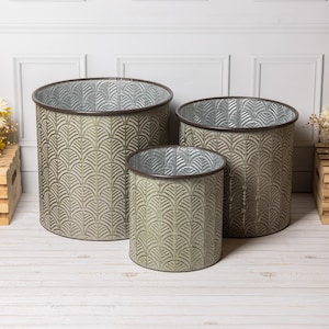 May include: A set of three metal planters in different sizes. The planters feature a textured, fan-shaped pattern in a muted green hue. Each planter has a dark brown rim and a silver interior. Suitable for indoor or outdoor use, these planters are ideal for gardens.