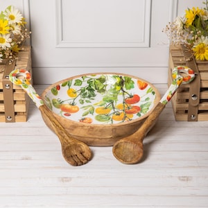Op de afbeelding: Een houten slakom met een tomatenrankenontwerp aan de binnenkant, vergezeld van een vork en een lepel. De handvatten van de gebruiksvoorwerpen hebben een bijpassend tomatenontwerp. De kom en het bestek zijn van hout.