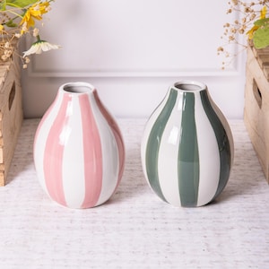Könnte beinhalten: Zwei Keramikvasen mit einem gestreiften Design. Eine Vase ist rosa und weiß, die andere grün und weiß.