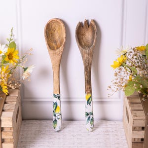 Può includere: Un set di due utensili da cucina in legno con manici a stampa di limone. Gli utensili sono un cucchiaio e una forchetta.