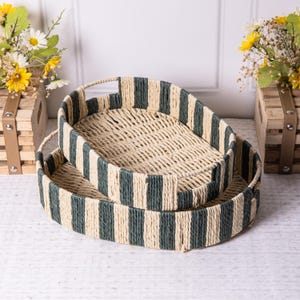 May include: Two oval-shaped woven trays with a striped pattern in beige and dark green. The trays are stacked on top of each other.