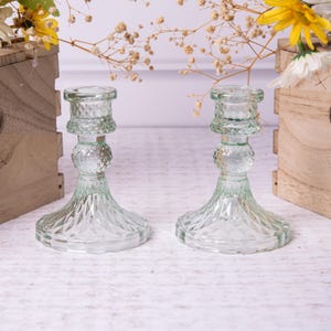 May include: Two clear glass candle holders with a diamond pattern. The candle holders are a light green colour and have a round base.