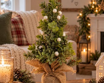 May include: A small artificial tabletop tree with green boxwood-style foliage and scattered white berries. The base of the tree is wrapped in natural tan burlap fabric, tied securely with a matching burlap cord to create a rustic, textured appearance.