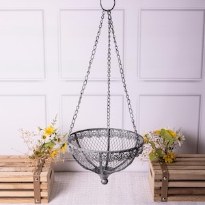 May include: A grey metal hanging basket with a decorative openwork design, suspended by chains. The basket has a round top with a decorative edge. Suitable for plants or decorative items, it is a stylish addition to any home.