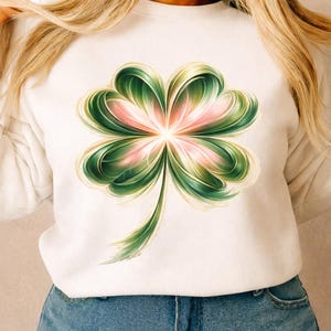 May include: White sweatshirt featuring a large, stylized four-leaf clover design. The clover has green and gold-toned leaves with a pink center, creating a vibrant and eye-catching graphic. The design is centered on the front of the sweatshirt.