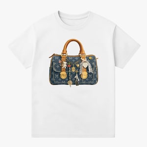 Op de afbeelding: Wit T-shirt met een denim-stijl handtas afbeelding. De tas heeft bruine handvatten en is versierd met bedels, waaronder een teddybeer, kersen en een hart. De tas heeft goudkleurige hardware en de letter "M" is op de tas gedrukt.
