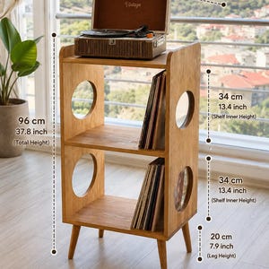 May include: A light brown wooden record player stand with two open shelves and circular side cutouts. It measures 19.6 inches wide, 15 inches deep, and 37.8 inches in total height, with 13.4-inch shelf heights and 7.9-inch legs.