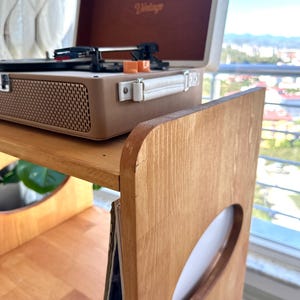 May include: A light brown wooden record player stand with oval cutouts on the side panels and a shelf for vinyl records. A beige and brown portable record player with the word Vintage printed on the inside lid sits on the top surface.