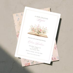 May include: A white bridal shower invitation card featuring a watercolor illustration of an open book with a bouquet of pink, white, and blue flowers emerging from the pages. The text reads A NEW CHAPTER BEGINS, Olivia Andrews, and event details.