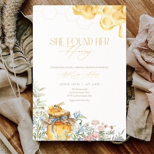 May include: A bridal shower invitation with the text "SHE FOUND HER Honey" in gold script. The invitation features watercolor illustrations of a honey jar, flowers, and a honeycomb design. The date and time of the event are also included.