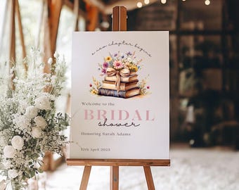 Pode incluir: Uma placa branca em um cavalete de madeira com o texto "a new chapter begins" e "Welcome to the BRIDAL shower". A placa apresenta uma ilustração em aquarela de livros e flores. A data "12th April 2023" também é exibida.