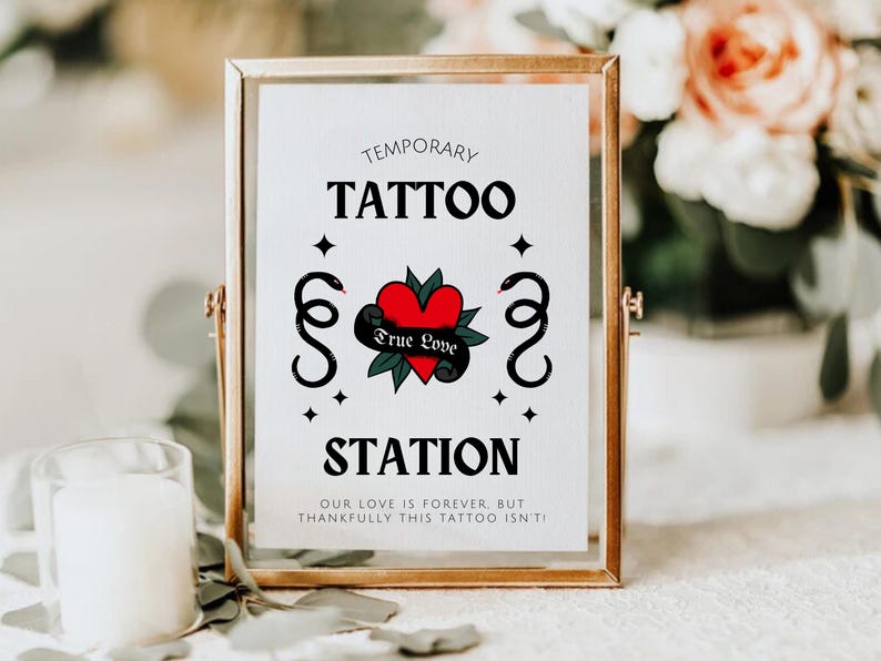 K&ouml;nnte beinhalten: Ein goldfarbener Rahmen mit dem Text "Temporary Tattoo Station" und einem roten Herzen mit den Worten "True Love" umgeben von Schlangen. Das Schild ist auf wei&szlig;em Hintergrund mit schwarzen Sternen.