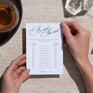 Puede incluir: Una tarjeta de juego de boda rectangular blanca titulada He said She said con texto negro y casillas de verificaci&oacute;n en forma de coraz&oacute;n. La tarjeta enumera preguntas sobre una pareja, incluyendo I said I love you first, I like to sleep in.