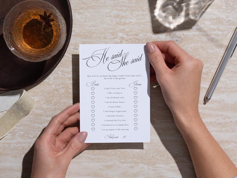 Puede incluir: Una tarjeta de juego de boda rectangular blanca titulada He said She said con texto negro y casillas de verificaci&oacute;n en forma de coraz&oacute;n. La tarjeta enumera preguntas sobre una pareja, incluyendo I said I love you first, I like to sleep in.