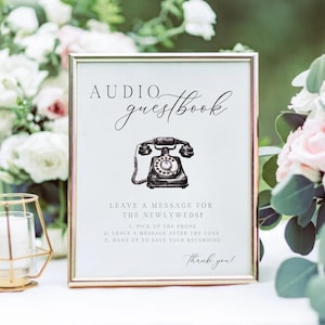 K&ouml;nnte beinhalten: Ein gerahmtes Schild mit goldenem Rand, das die Worte "Audio Guestbook" in Schreibschrift &uuml;ber einer Vintage-Telefonillustration zeigt. Anweisungen sind unter dem Bild angegeben, mit einem "Danke!" am unteren Rand. Das Schild steht vor einem Hintergrund aus Blumen.