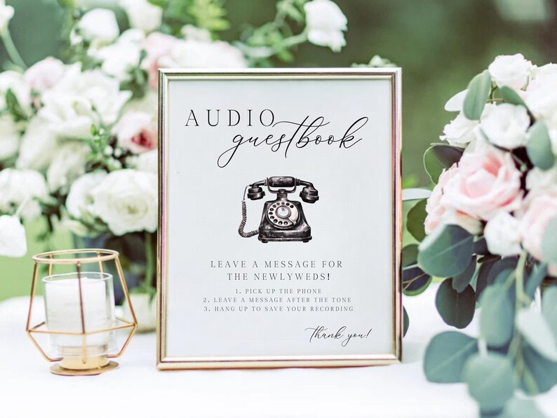 K&ouml;nnte beinhalten: Ein gerahmtes Schild mit goldenem Rand, das die Worte "Audio Guestbook" in Schreibschrift &uuml;ber einer Vintage-Telefonillustration zeigt. Anweisungen sind unter dem Bild angegeben, mit einem "Danke!" am unteren Rand. Das Schild steht vor einem Hintergrund aus Blumen.