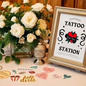 K&ouml;nnte beinhalten: Ein Schild f&uuml;r eine tempor&auml;re Tattoo-Station auf einer Hochzeit. Das Schild ist golden mit wei&szlig;em Hintergrund und tr&auml;gt die Aufschrift "Temporary Tattoo Station" mit einem Herz und den Worten "True Love".