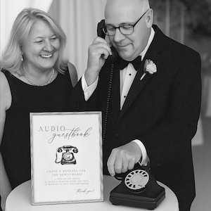 K&ouml;nnte beinhalten: Schwarz-Wei&szlig;-Bild eines Audio-G&auml;stebuchs f&uuml;r Hochzeiten. Ein gerahmtes Schild mit den Worten "Audio Guestbook" und Anweisungen steht vor einem schwarzen Vintage-Drehtelefon. Ein Mann im Smoking h&auml;lt das Telefon an sein Ohr.