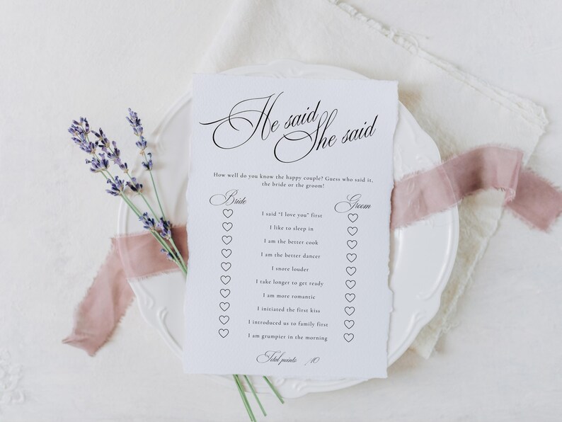 Puede incluir: Una tarjeta de juego rectangular blanca con bordes irregulares que presenta el texto negro He said She said y una lista de preguntas con casillas de verificaci&oacute;n en forma de coraz&oacute;n. La tarjeta est&aacute; sobre un plato blanco con lavanda y cinta rosa.