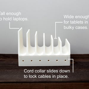 May include: White plastic stand with six slots for holding devices like laptops and tablets. The stand has a cord collar that slides down to lock cables in place. "Tall enough to hold laptops. Wide enough for tablets in bulky cases. Cord collar slides down to lock cables in place."