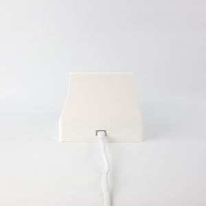 May include: A white, rectangular charging base with a white cord attached. The base has a slightly curved top and a flat bottom.