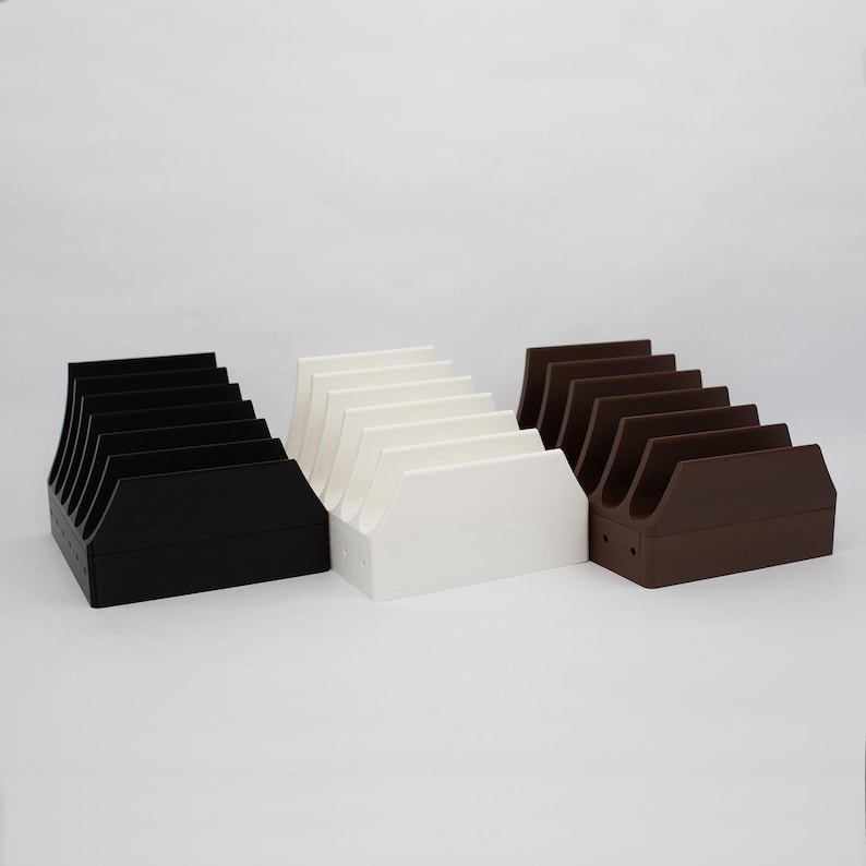 May include: Three different colored plastic storage organizers for video game cartridges. The organizers are black, white, and brown. Each organizer has six slots for cartridges.
