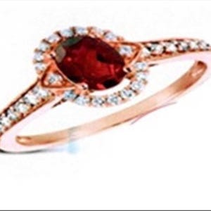 May include: Rose gold ring featuring a large oval-cut, deep red gemstone surrounded by a halo of smaller, clear gemstones. The band is also adorned with smaller gemstones, creating a sparkling effect. A classic and elegant piece of jewelry.