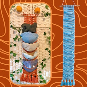 Op de afbeelding: Twee verticale gehaakte wandorganizers voor petten. De ene is oranje met vijf gestapelde baseballpetten in olijfgroen, lichtblauw, beige, wit en grijs. De andere is lichtblauw met een rasterpatroon. Beide hebben houten stokken en kwastjes onderaan.