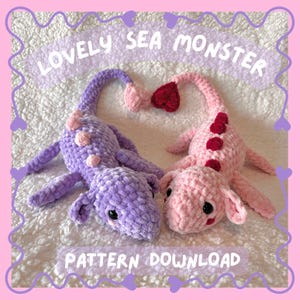 Op de afbeelding: Twee gehaakte zeemonster knuffels, één paars en één roze, met harten op hun staarten. De tekst "LOVELY SEA MONSTER PATTERN DOWNLOAD" staat bovenaan en onderaan de afbeelding.