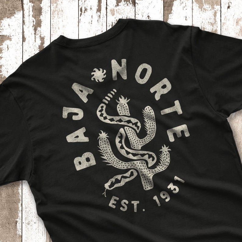 May include: Black t-shirt with a distressed white graphic featuring a snake intertwined with cacti, and the words "BAJA NORTE EST. 1931". The design has a vintage, desert-inspired aesthetic.
