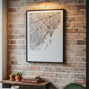 May include: A framed black and white map print of Barcelona, Spain, featuring a detailed street grid and coastline. The text at the bottom reads BARCELONA, SPAIN, followed by coordinates. The print is displayed on a rustic red brick wall.
