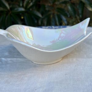 May include: A white iridescent ceramic bowl shaped like a leaf with a small spout on one side.
