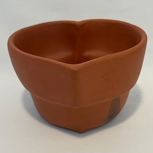 May include: A small, heart-shaped terracotta pot with a warm, earthy brown color. The pot has a slightly rough texture and a simple, geometric design. The interior is smooth and empty.
