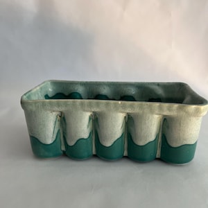 以下が含まれることがあります： 薄い緑とターコイズの釉薬をかけた長方形のセラミックプランター。プランターは上縁に波状のデザインと、底に丸い窪みが並んでいます。