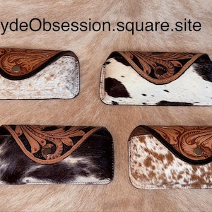 May include: Four eyeglass cases with cowhide patterns. Each case has a brown leather top with a floral design and a snap closure. The cowhide patterns vary in color, including white, brown, and black.