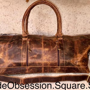May include: A brown leather duffel bag with two top handles and a detachable shoulder strap. The bag has two zipped pockets on the front and a distressed finish. The text "HydeObsession.Square.Site" is at the bottom.