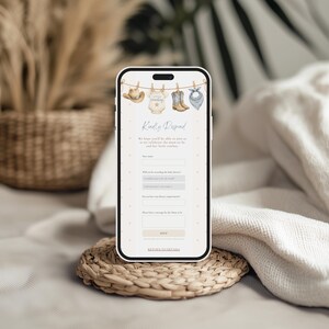 May include: A smartphone displaying a digital baby shower RSVP form with a western theme. The top features a clothesline illustration with a cowboy hat, a onesie labeled little cowboy, boots, and a bandana. The form includes fields for name, attendance, dietary requirements, and a message.