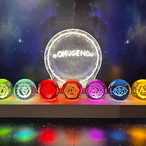 May include: A display of seven illuminated glass spheres, each with a different color and chakra symbol. The spheres are arranged on a wooden base, with a glowing circular sign that reads "OMUGENOO" in white. The background is a starry night sky.