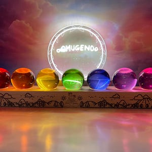 May include: A wooden display shelf holds seven illuminated glass spheres in a rainbow of colors: red, orange, yellow, green, blue, purple, and pink. The spheres are lit from within, creating a vibrant glow. The shelf has a decorative mountain and tree design.
