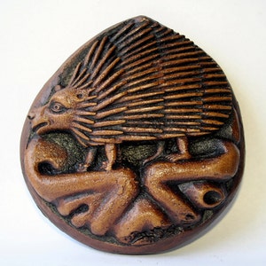 May include: A brown ceramic wall plaque depicting a stylized hedgehog with spiky quills, standing on a curled, leafy branch.