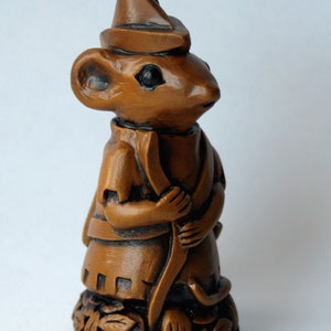 May include: A brown ceramic figurine of a mouse wearing a hat and holding a bow and arrow. The mouse is standing on a base with leaves.