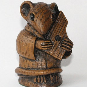 Könnte beinhalten: Eine Holzfigur eines Mause, das ein Musikinstrument spielt. Die Maus ist braun und hat einen langen Schwanz. Das Instrument ist eine kleine, rechteckige Harfe mit Saiten. Die Figur ist handgeschnitzt und hat ein rustikales Aussehen.