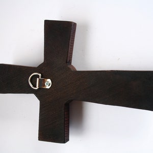 Pu&ograve; includere: Una croce di legno marrone scuro con un gancio di metallo per appendere sul retro.