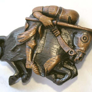 May include: A wooden sculpture of a knight on horseback, the knight is leaning forward and the horse is rearing up, both are painted in shades of brown and black.