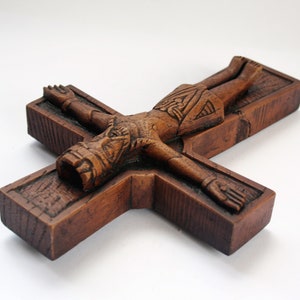 Pu&ograve; includere: Un crocifisso in legno con una figura scolpita di Ges&ugrave; Cristo. La figura &egrave; dettagliata con una corona di spine e un perizoma. La croce &egrave; in legno marrone scuro e ha una finitura rustica.