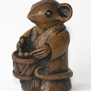 Könnte beinhalten: Eine braune Holzfigur eines Mause, das Trommel spielt. Die Maus trägt eine Robe und hat einen langen Schwanz.
